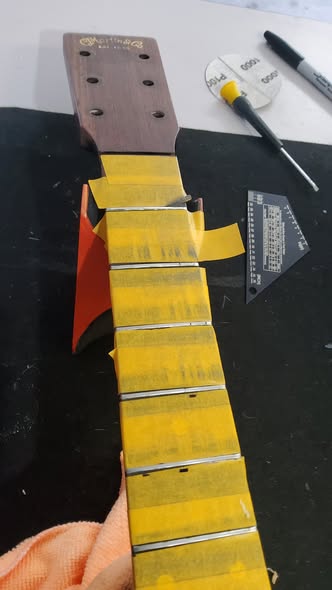 Martin acoustic neck with frets masked in yellow tape, prepped for leveling and crowning on the workbench